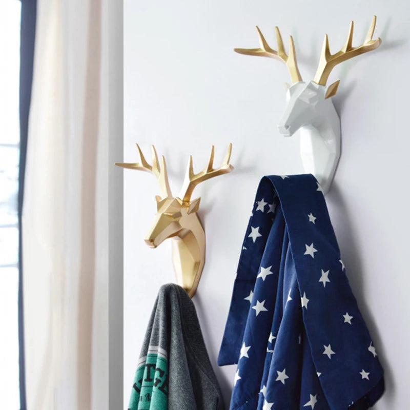 Decorative deer head wall hooks with a blue blanket and gray jacket on a white wall.