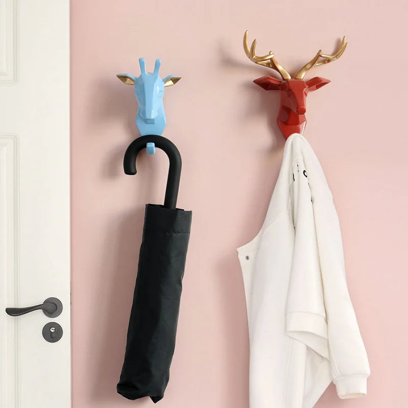 Two decorative wall hooks shaped like animal heads with a black umbrella and white coat hanging on them against a pink wall.