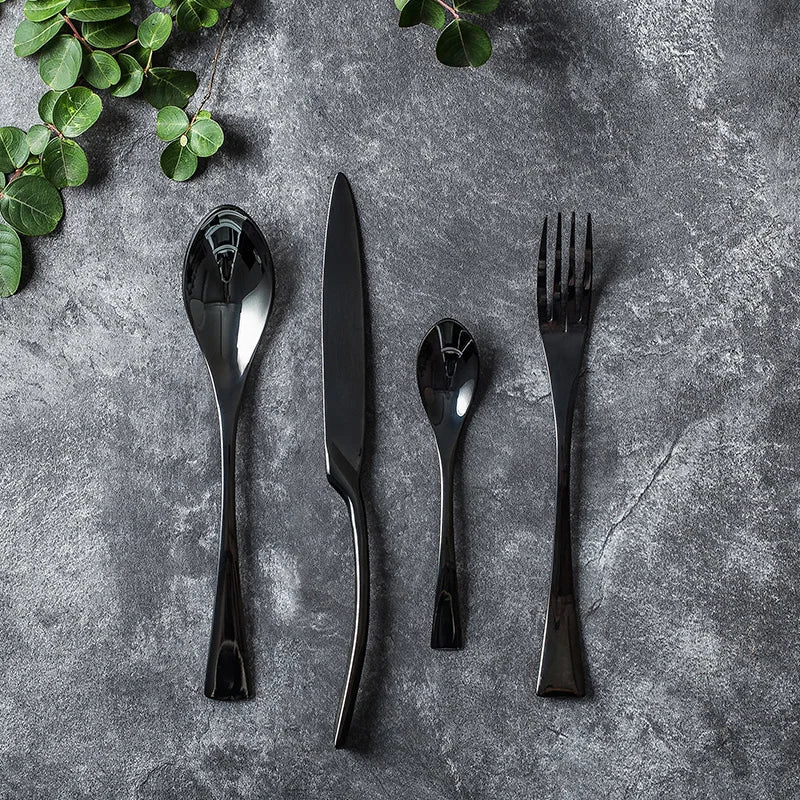 Set of black cutlery on a gray stone surface with green leaves.