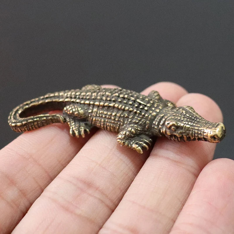Bronze alligator figurine held in a hand against a dark background