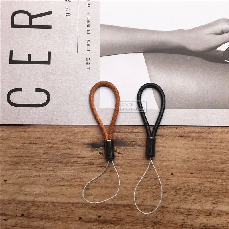 Two leather straps, one brown and one black, on a wooden surface with a magazine in the background.