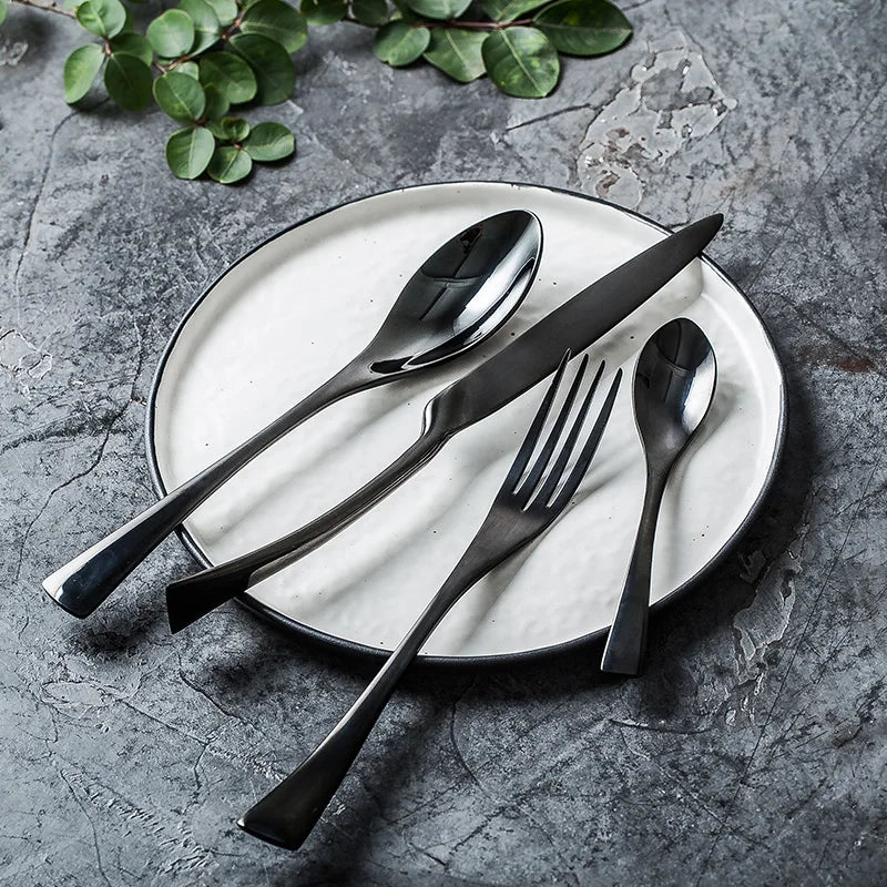 Set of black cutlery on a white plate with green leaves on a gray surface