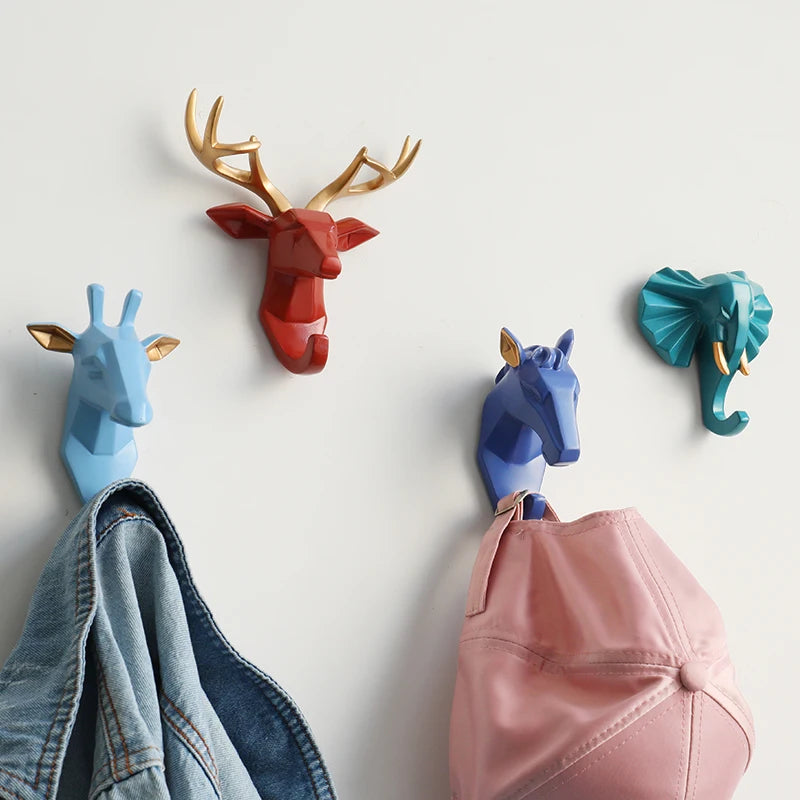 Four colorful animal head-shaped hooks on a white wall with clothes hanging from them.