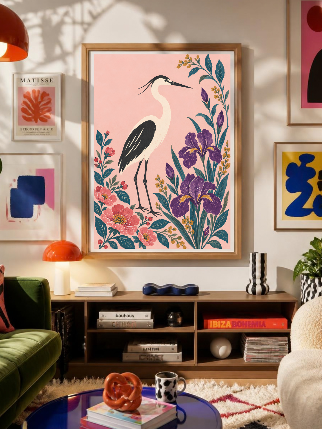 A framed art print featuring a pink heron with purple irises and green foliage, displayed on a wall in a modern living room setting.