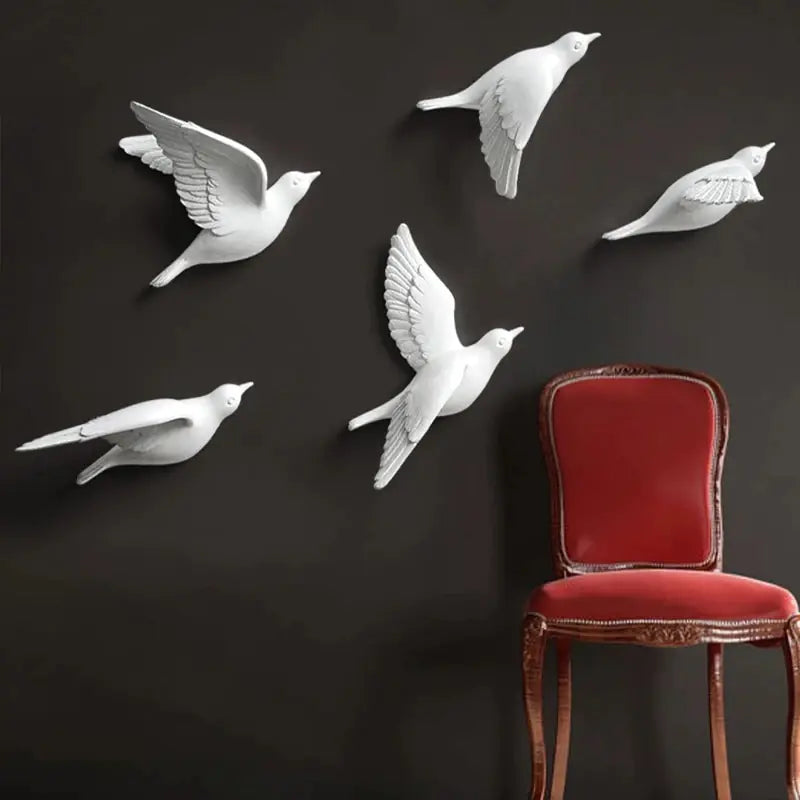 White bird wall decorations on a dark wall with a red chair.
