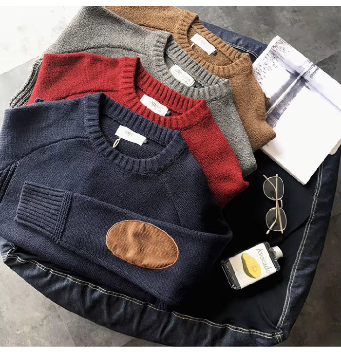 Stack of folded sweaters with a denim jacket, sunglasses, and a bottle on a gray surface