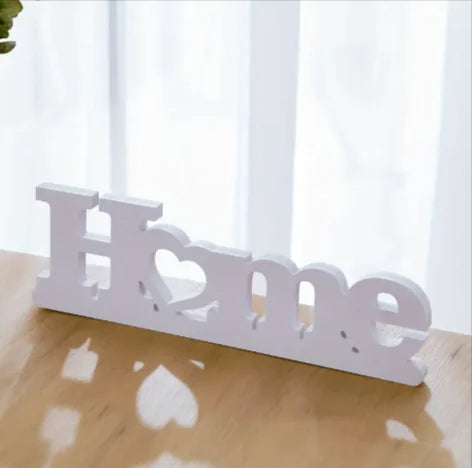 White decorative sign with 'Home' and heart design on a wooden surface.