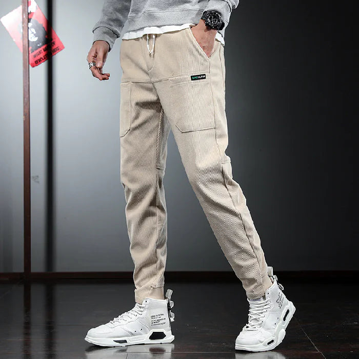 Person wearing beige cargo pants and white sneakers on a dark floor.