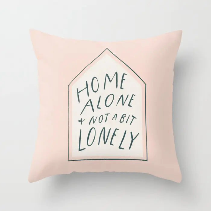 Pink pillow with text 'Home alone & not a bit lonely' on a light gray background