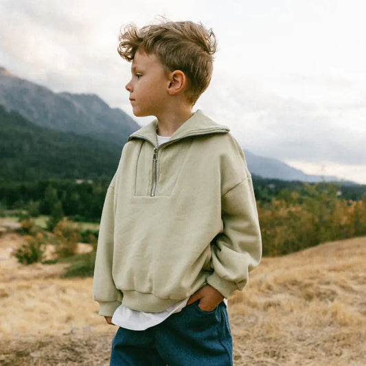 Child wearing a beige pullover in a mountainous landscape
