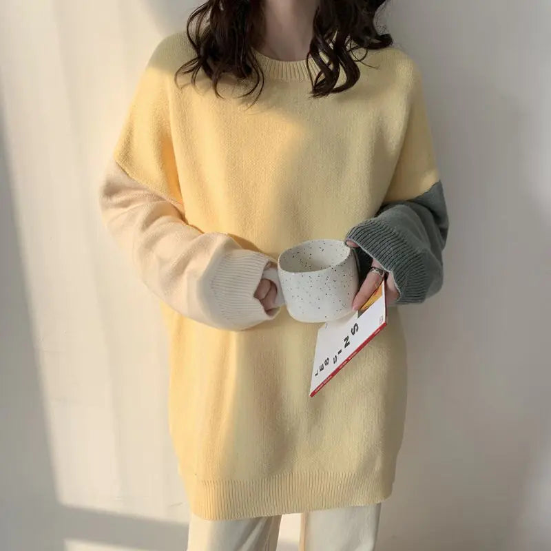 Person wearing a yellow sweater holding a white mug with a red label against a plain background