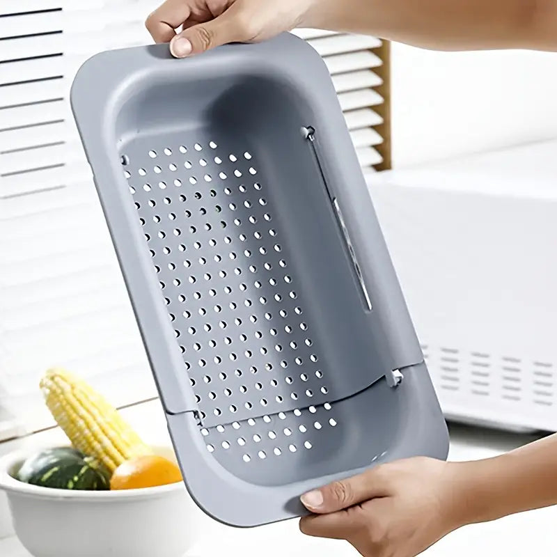 Gray kitchen tool with perforated design held by a person, with vegetables in the background.