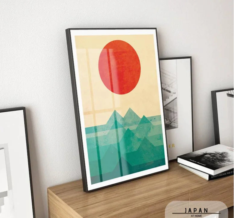 Framed abstract art print with a red circle and green mountains on a beige background, displayed on a wooden shelf.