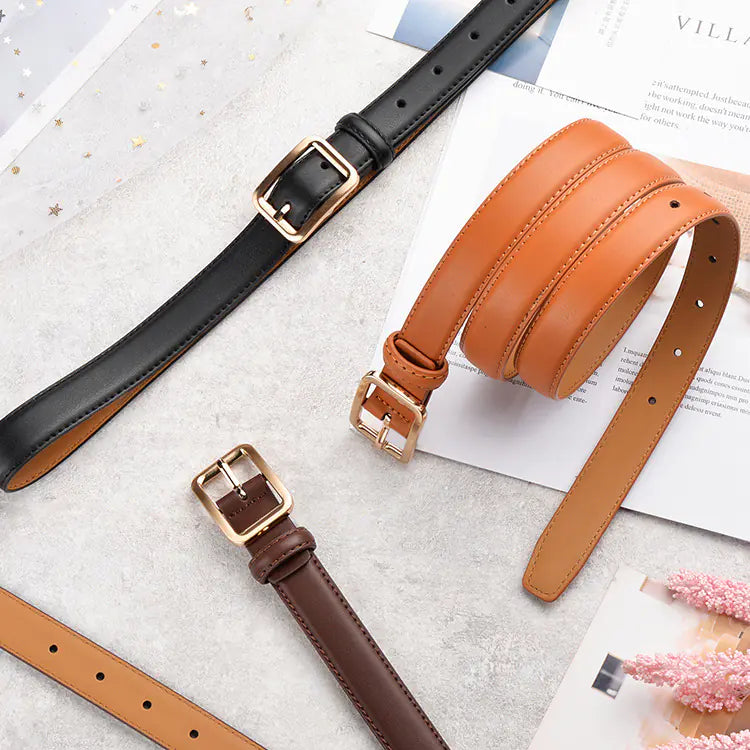 Four leather belts in black, brown, and tan on a textured surface with a magazine underneath.