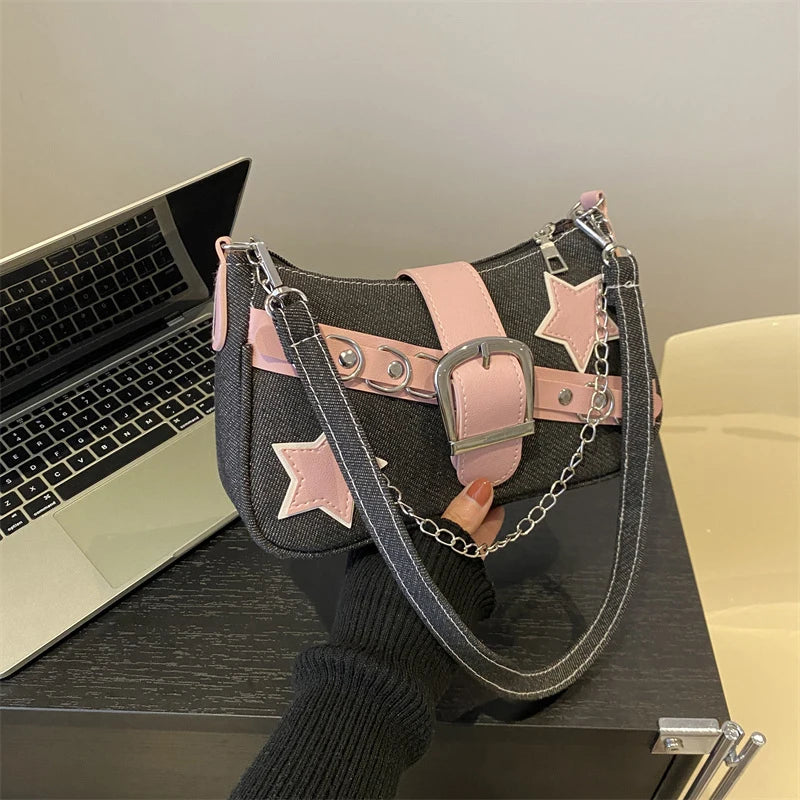 Black handbag with pink stars and chain detail on a desk next to a laptop.