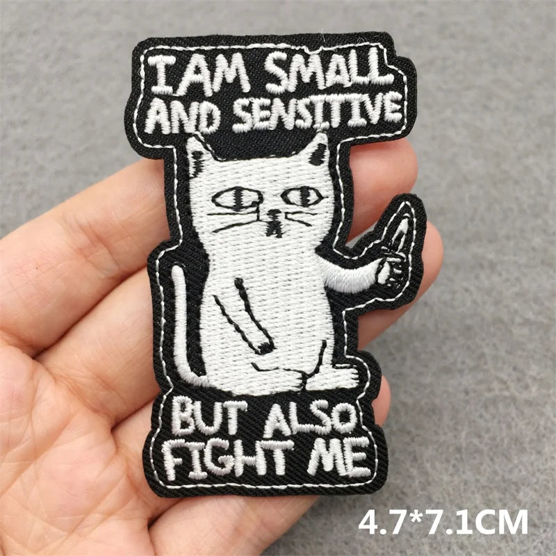 Embroidered patch with a cat design and text held in a hand on a gray background