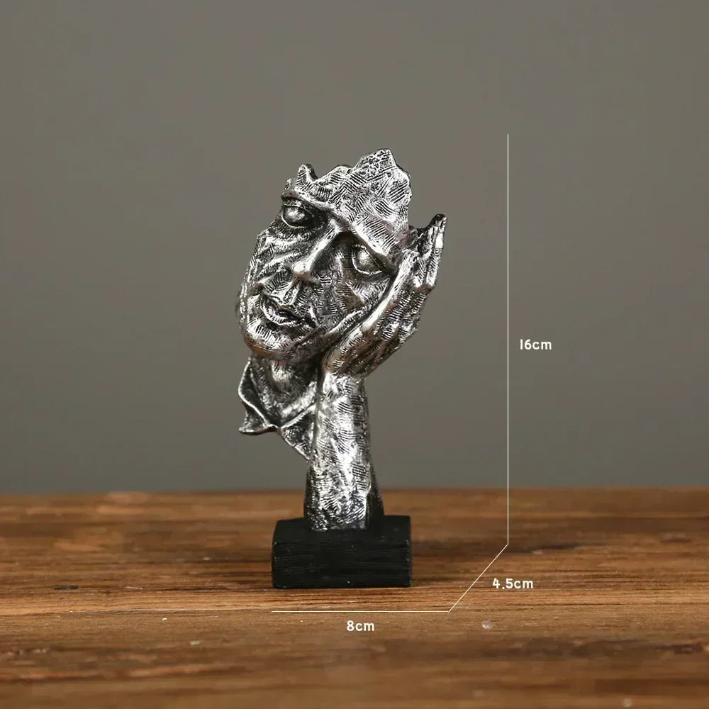 Silver sculpture of a face on a wooden surface with measurements indicated