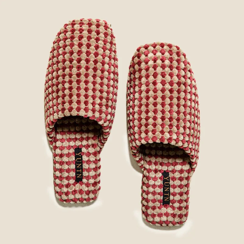 A pair of slip-on slippers with a textured geometric pattern in red and cream, displayed on a light beige background. The brand name 'YUNIN' is visible on black labels on the soles.