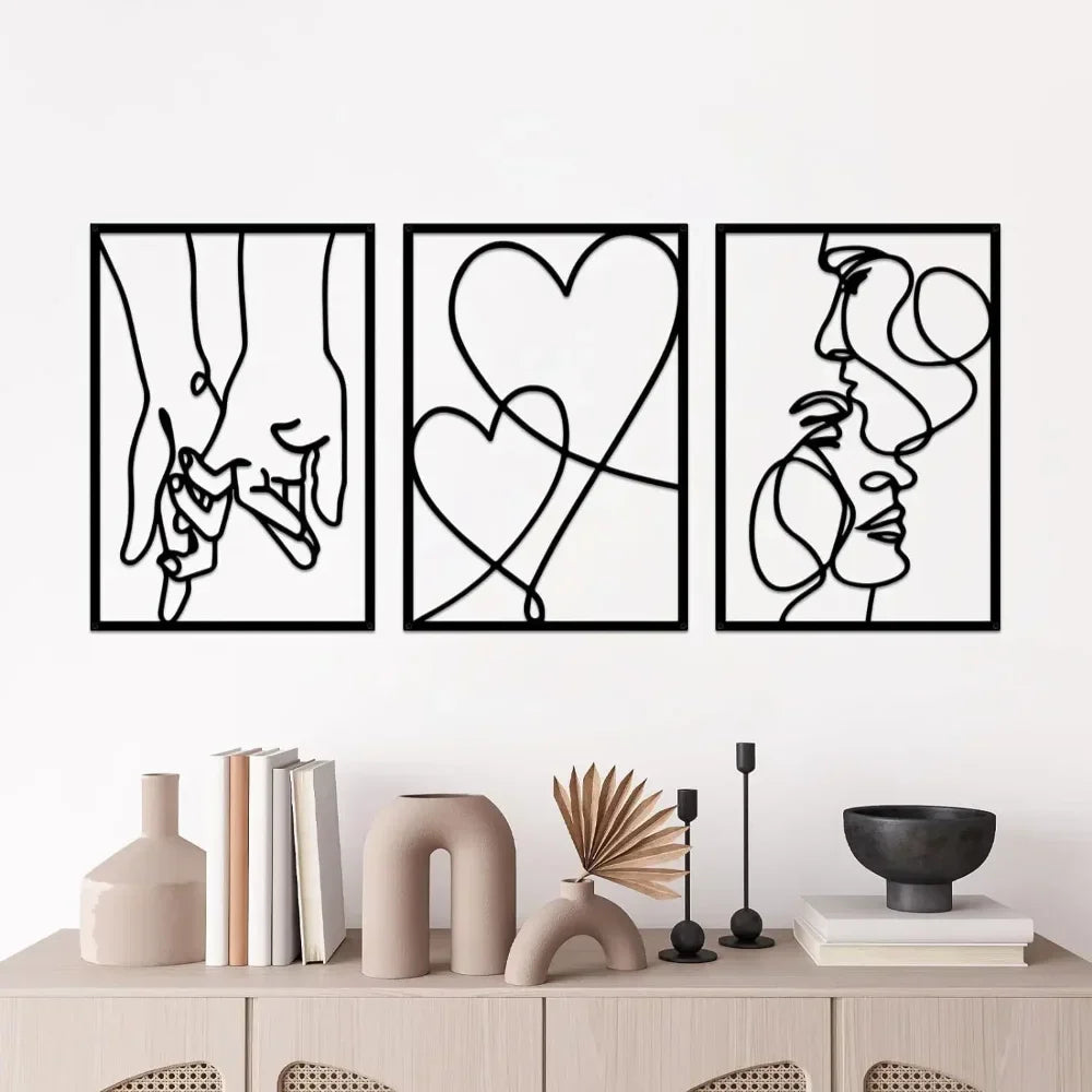 Three black and white metal abstract wall art pieces on a white wall above a wooden cabinet with decorative items.