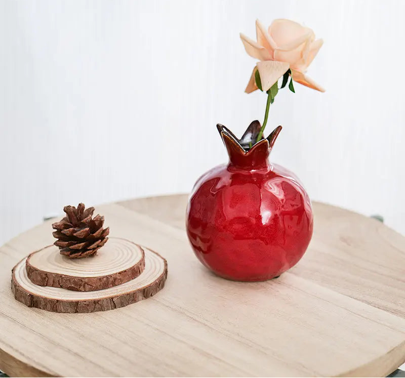 Red pomegranate vase with a flower on a wooden surface,  