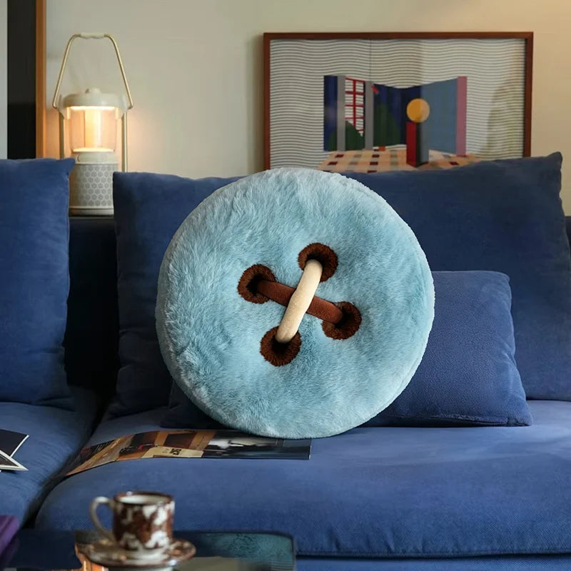 Round blue pillow with a brown button on a blue sofa in a living room.