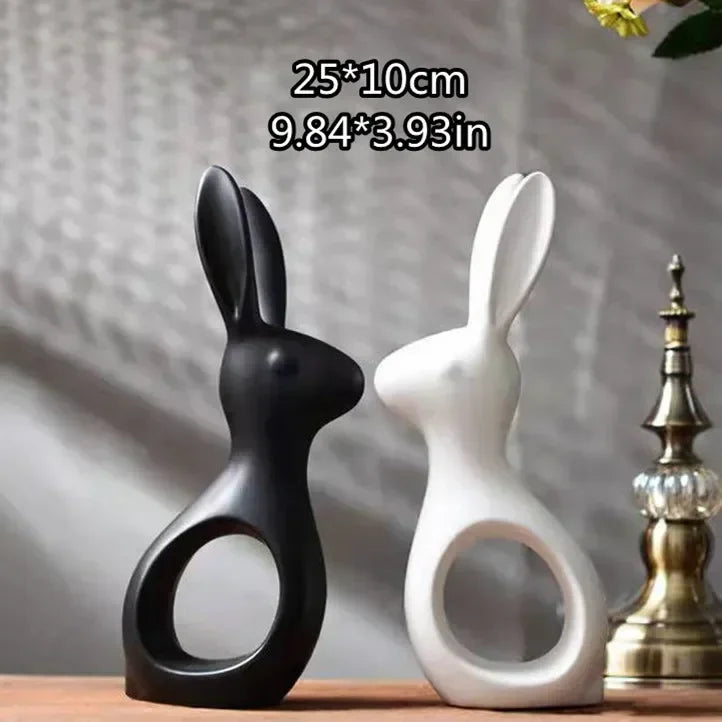 Two ceramic rabbit sculptures, one black and one white, on a wooden surface with a blurred background.
