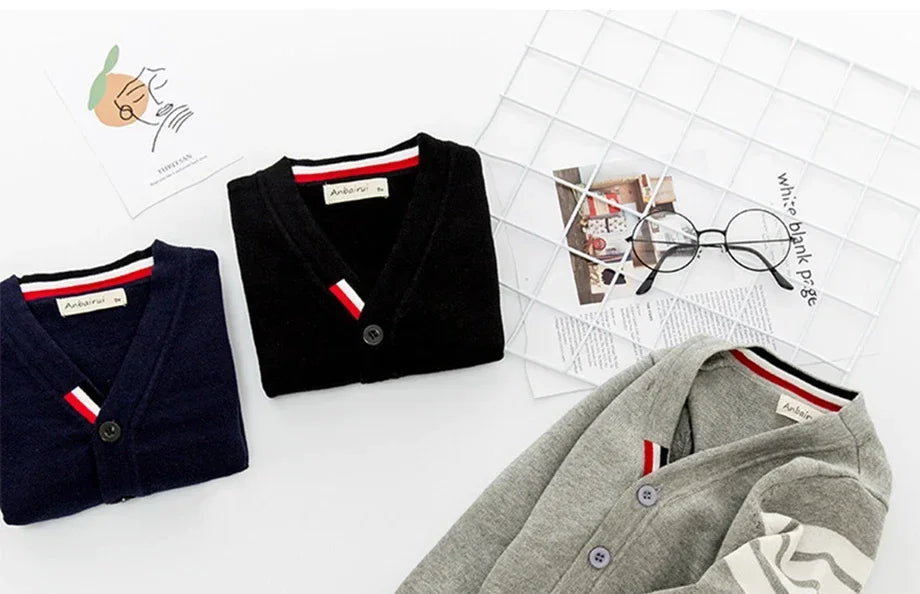 Three cardigans in black, gray, and navy on a white surface with a magazine and glasses in the background.