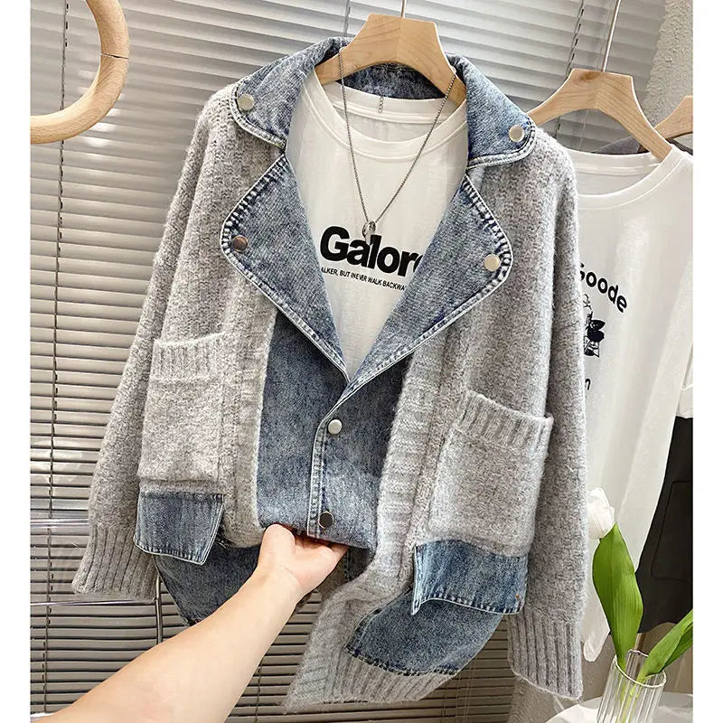 Gray cardigan with denim accents held by a hand, with a blurred background