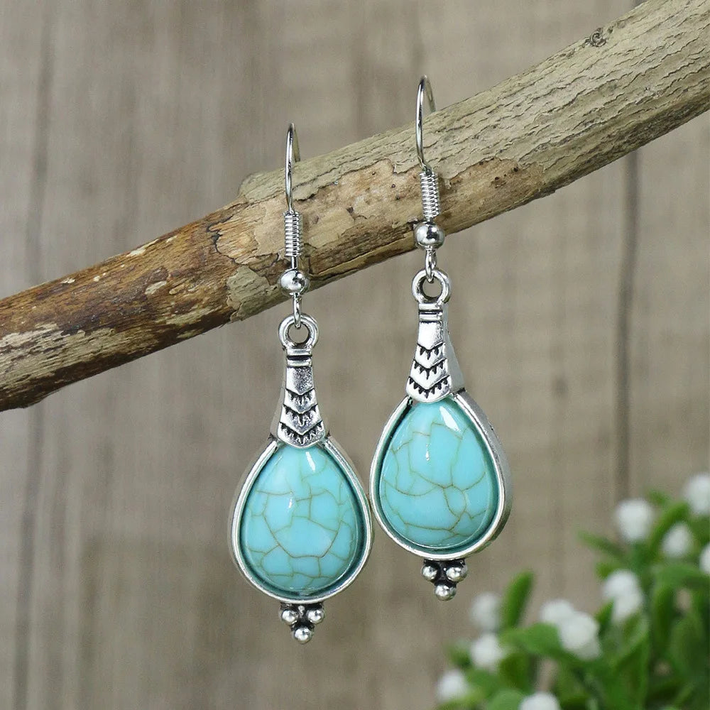 Turquoise teardrop earrings with silver hooks on a wooden branch.