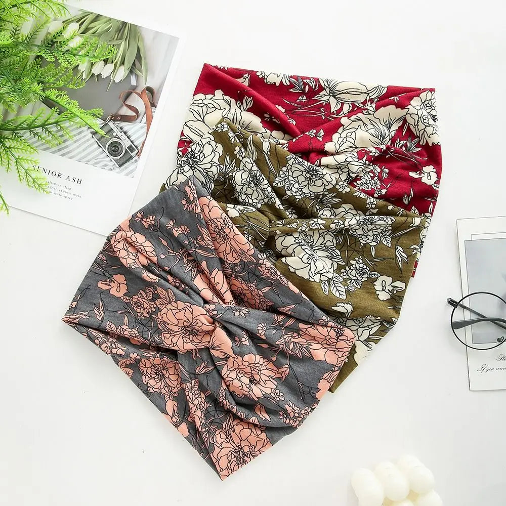 Three floral-patterned scarves in red, green, and gray on a white surface with a magazine and glasses.