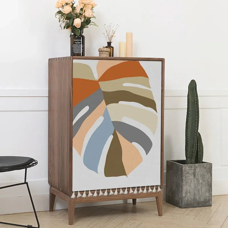Wooden cabinet with abstract design next to a cactus plant and flowers on a white wall.