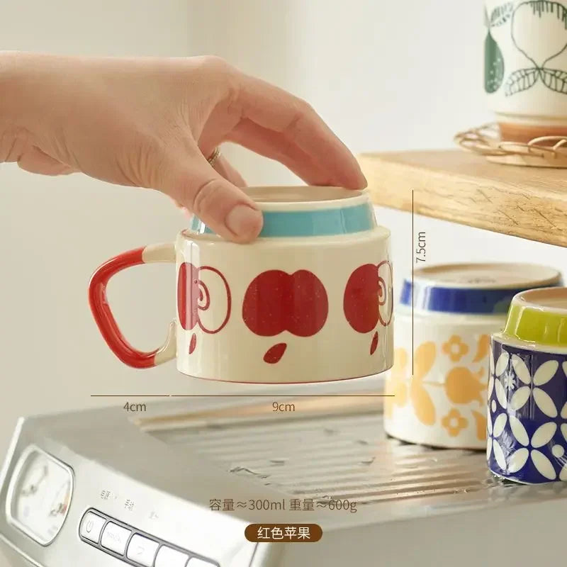 Hand holding a ceramic mug with red apple design on a kitchen counter.