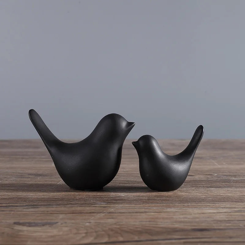Two black ceramic bird sculptures on a wooden surface with a gray background