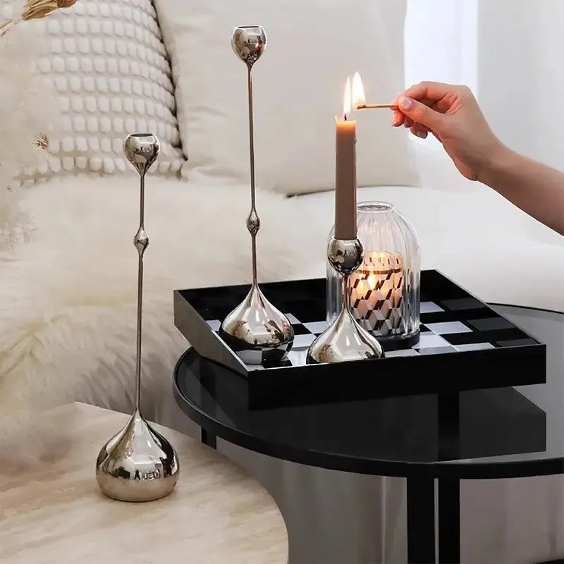 Person lighting a candle on a decorative tray with silver candle holders and a checkered pattern.
