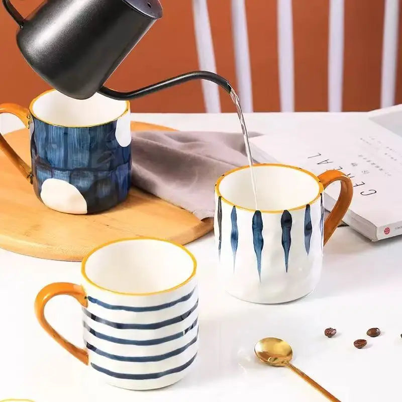 Two ceramic mugs with striped patterns on a table with a book and coffee beans.