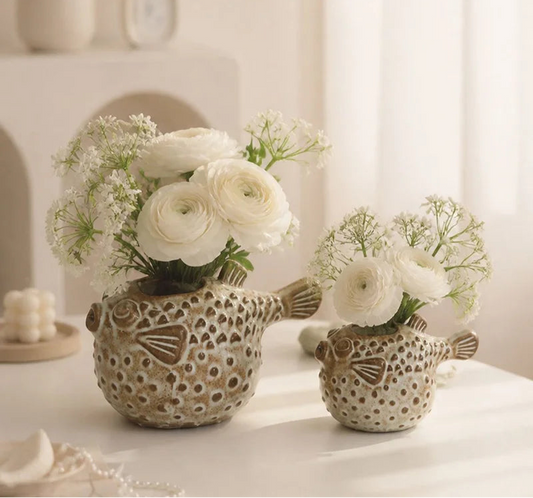 Large and small ceramic pufferfish vases with rustic glazed finish displayed with white flowers on a table.