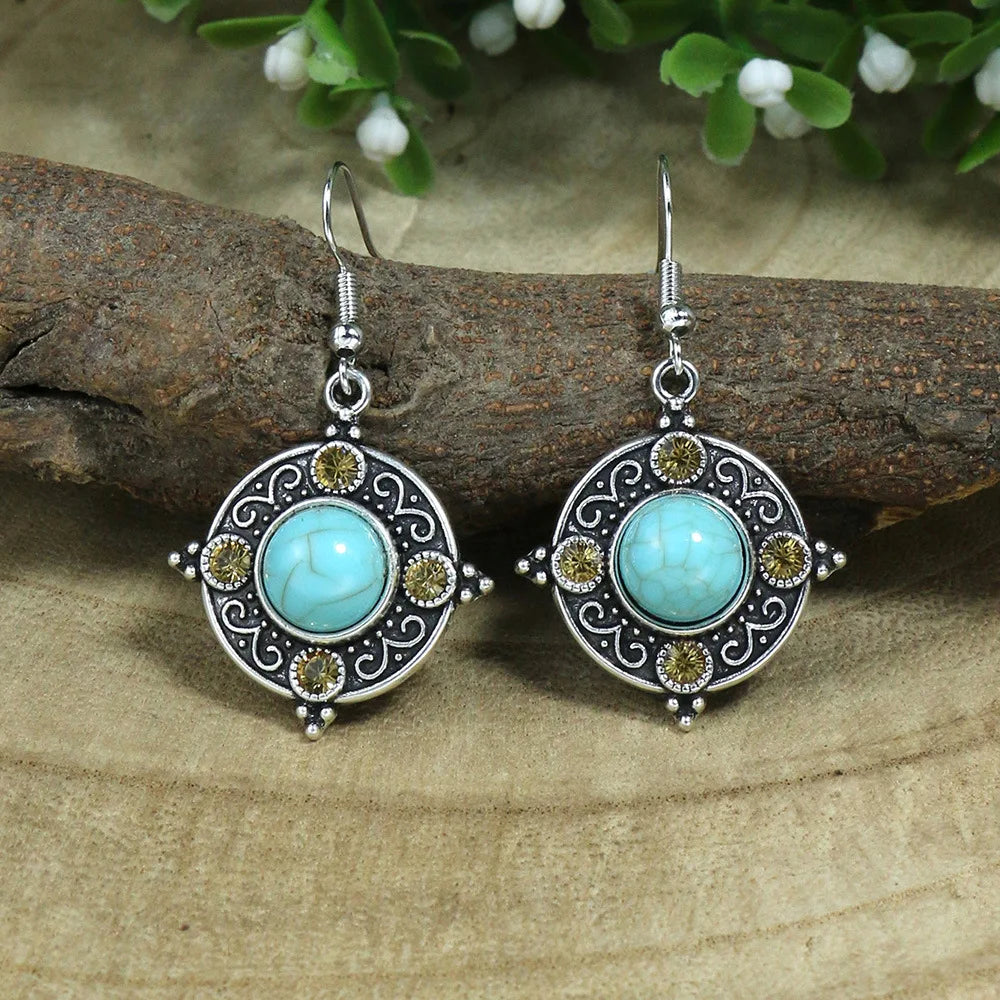 Pair of turquoise stone earrings with silver and gold accents on a wooden surface.