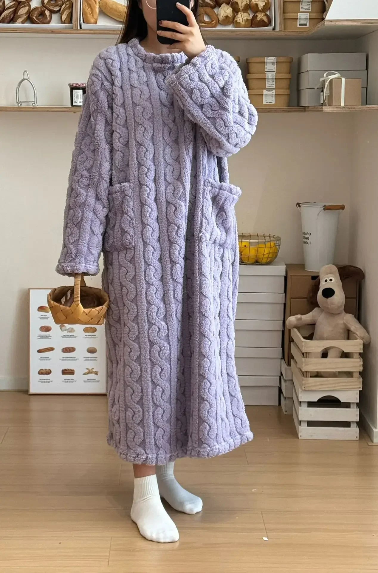 Person wearing a long cable knit robe in a room with shelves and a teddy bear.
