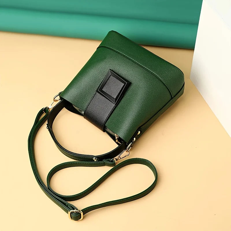 Green handbag with a black strap on a beige surface with a teal background
