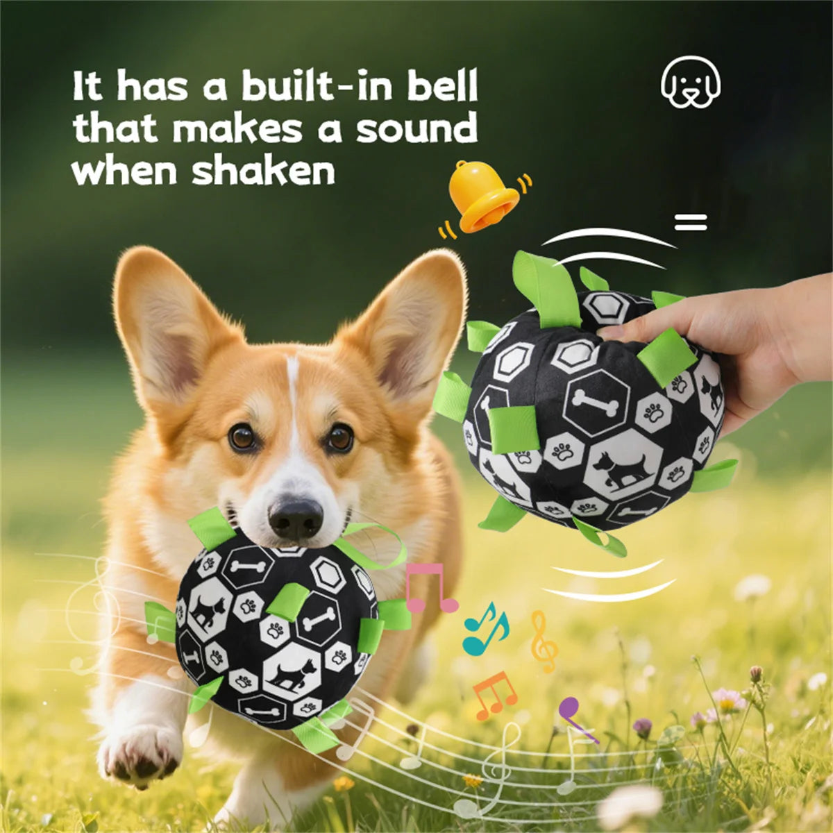 Dog playing with a black and white ball toy with a built-in bell, set against a blurred green outdoor background.