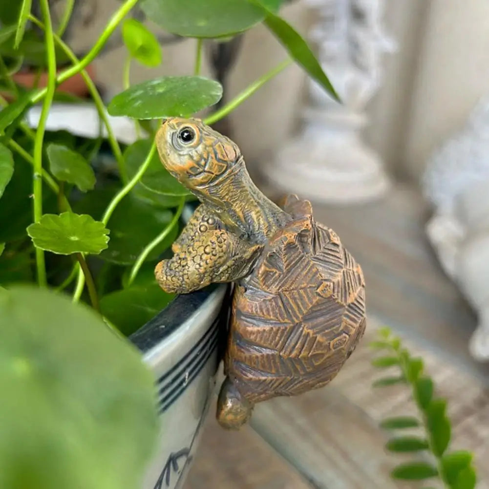 Bronze turtle figurine on a plant pot with green leaves in the background