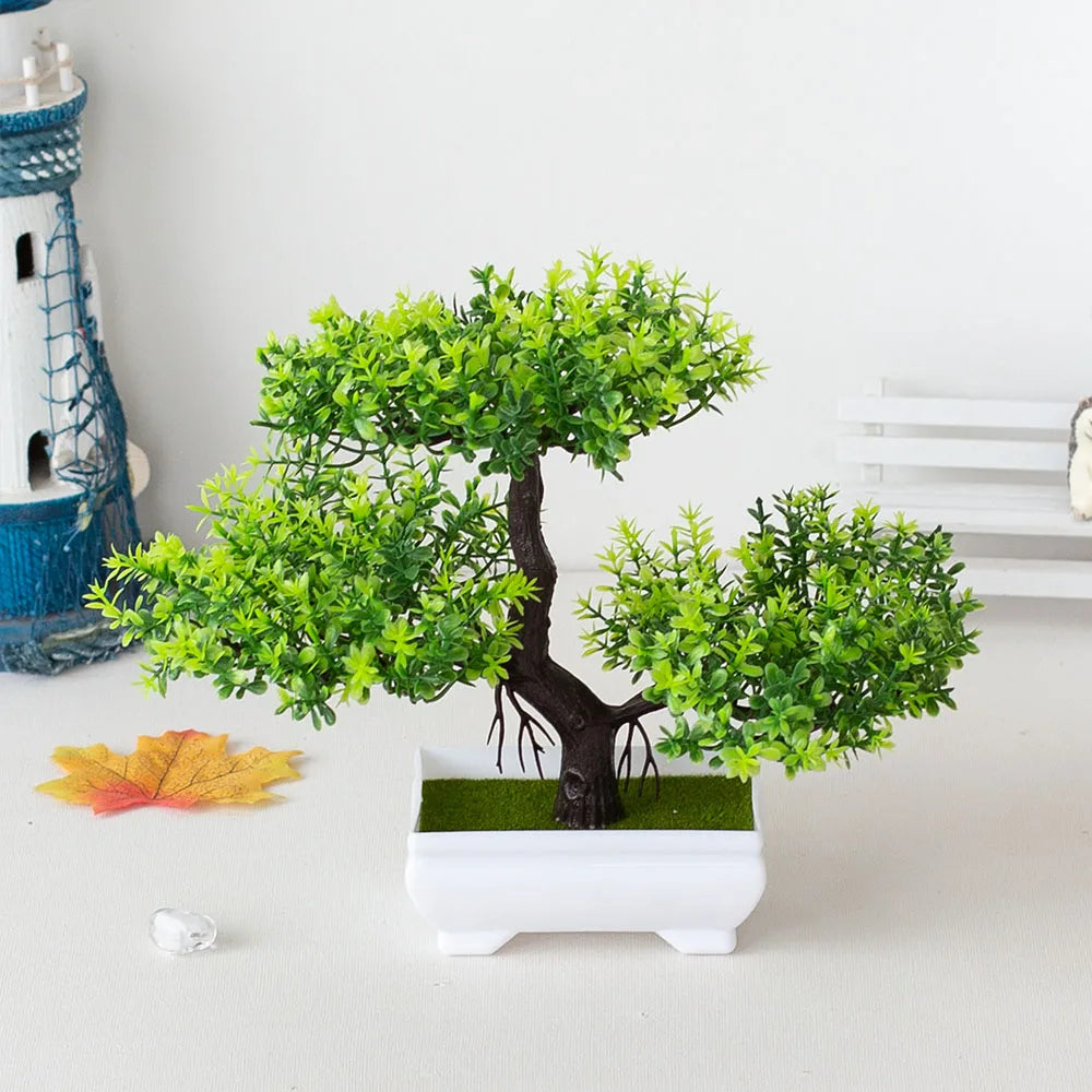 Artificial bonsai tree in a white pot on a light surface with decorative elements.