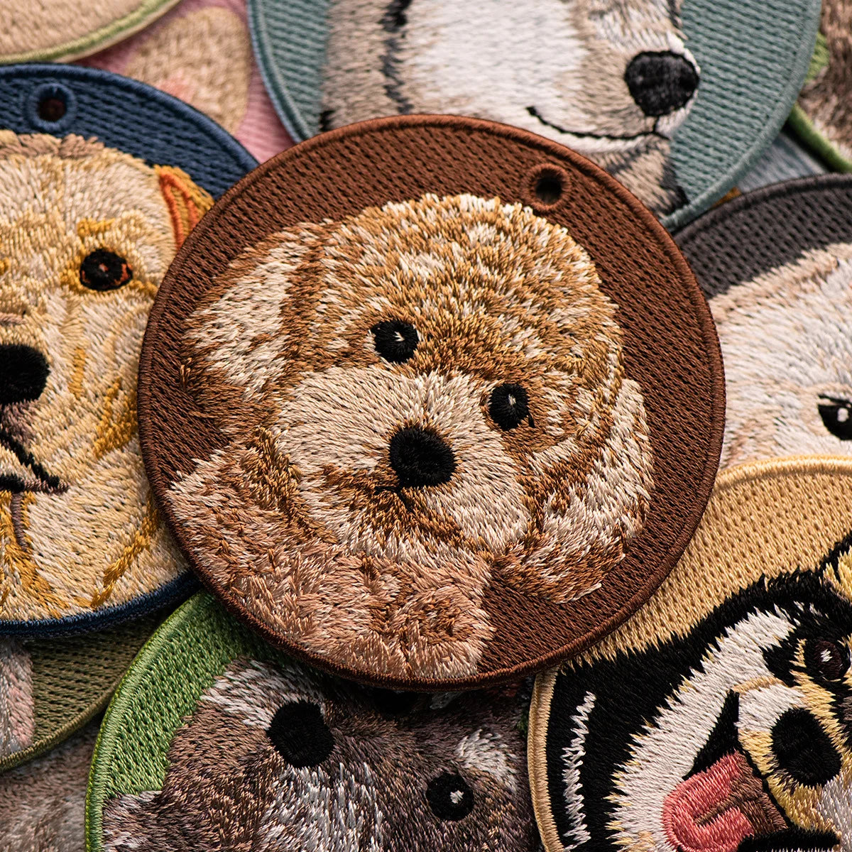 Collection of embroidered patches featuring animal faces, including a bear and dog, on a textured fabric background.