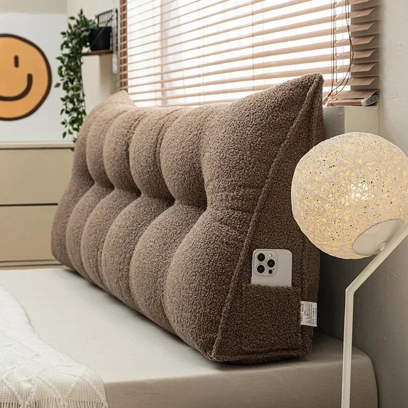 Brown plush headboard pillow on a bed with a lamp and window blinds in the background