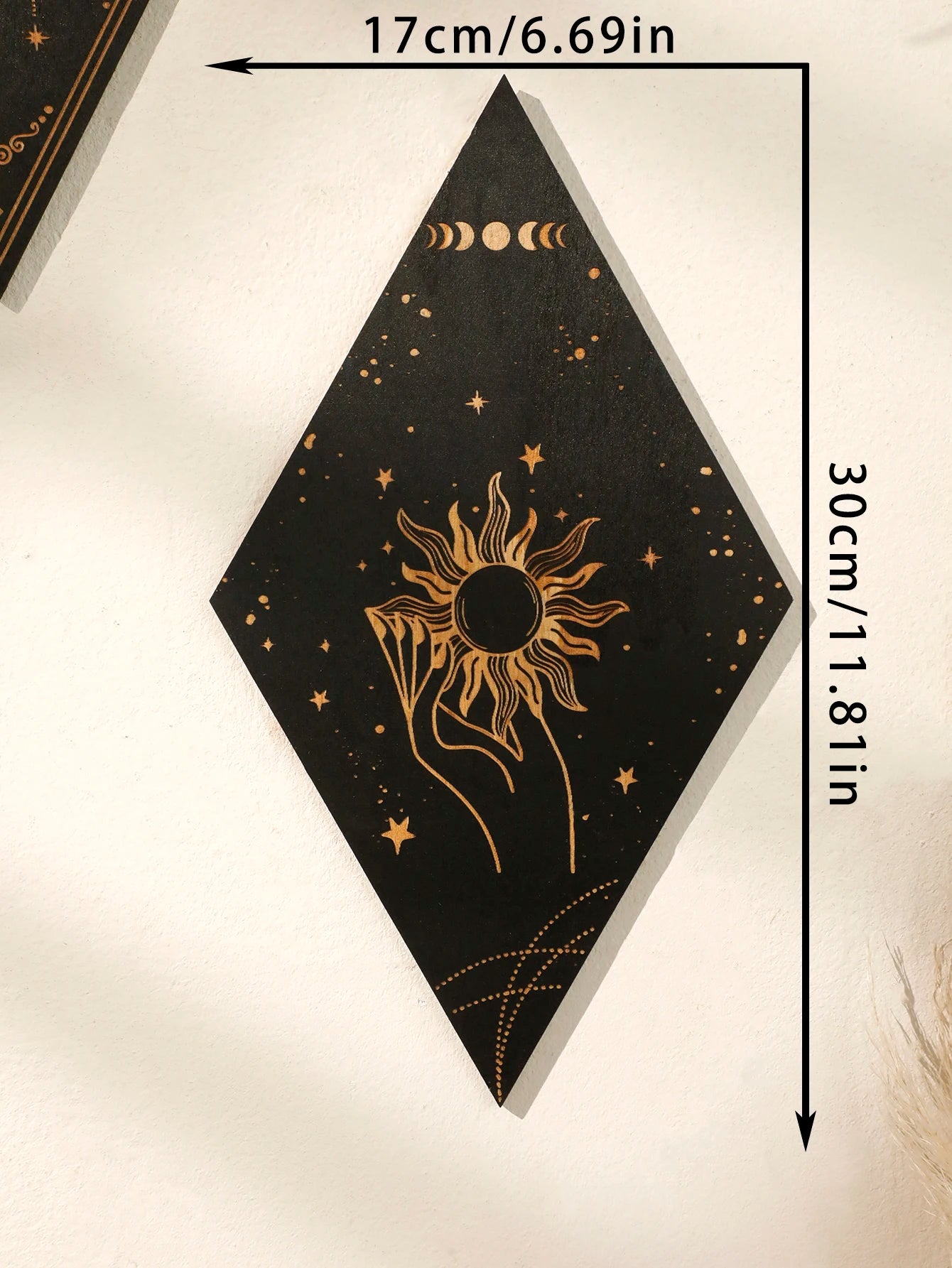 A black diamond-shaped wall art piece with gold celestial designs, including a sun, moon phases, stars, and a hand, shown with dimension arrows and text indicating 17cm by 30cm.
