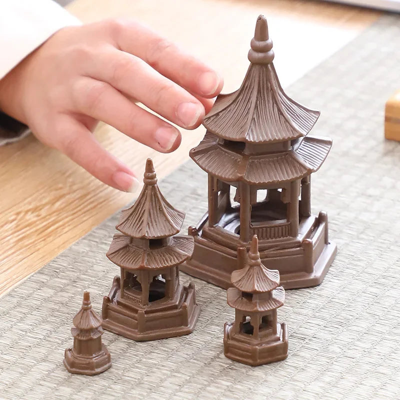 Set of small brown pagoda models on a textured surface with a hand reaching towards one of them.