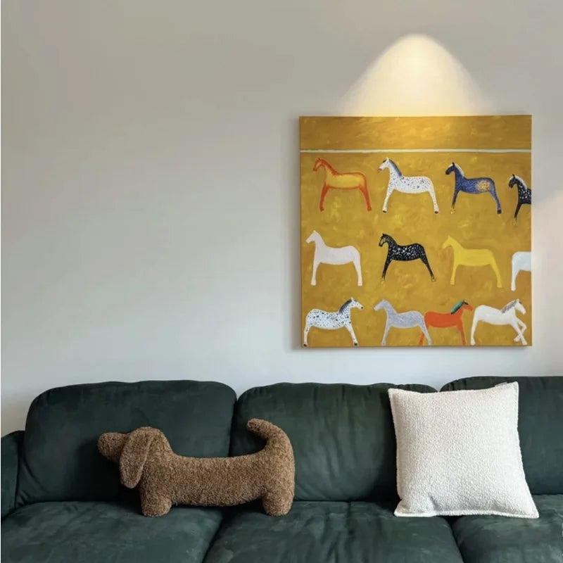 dachshund-shaped cushion on a Green sofa with decorative pillows and a painting of horses on the wall.