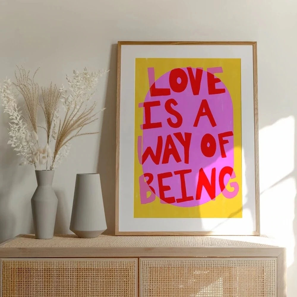 Framed artwork with 'Love is a Way of Being' text on a wooden cabinet with decorative vases.
