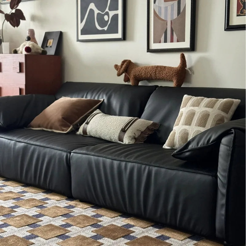 dachshund-shaped cushion on a Black leather sofa with decorative pillows in a living room setting.