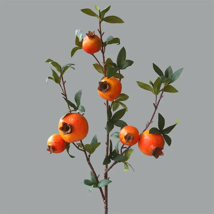Artificial pomegranate branch with green leaves on a gray background